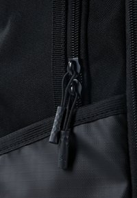 Primer plano de una bolsa de nailon negro con un cierre de cremallera bidireccional, tiradores texturizados, una superficie lisa y costuras reforzadas para mayor durabilidad.