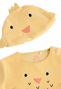 Gelbes Kleinkinder-Outfit aus flauschigem Material mit einem Küken-Design, kurzen Ärmeln und Druckknöpfen an der Schulter. Inklusive passendem Hut.