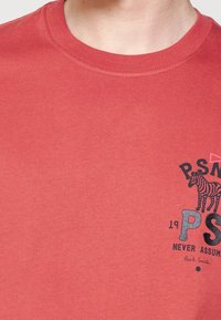 Camiseta de algodón roja con mangas cortas, con un escote redondo y un estampado gráfico negro de una cebra y texto en la parte frontal.