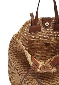Sac cabas en paille tissée avec des poignées en cuir marron, fermature magnétique et une poche intérieure tissée sur fond blanc.