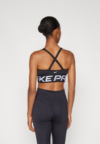 Fekete sportmelltartó keresztpántokkal és fehér "FAKE PRO" felirattal. Magas derekú fekete leggings-szel viselve, sima textúrával és testhezálló dizájnnal.