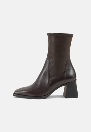 Stivale alla caviglia in pelle marrone con tacco quadrato, superficie in maglia aderente, punta affusolata e finitura liscia. Il dettaglio delle cuciture laterali arricchisce il design.
