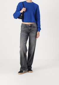 Maglione azzurro a maglia, cropped, con maniche lunghe, abbinato a jeans grigi a vita alta e gamba larga, e sneakers nere. Piccola borsa nera.