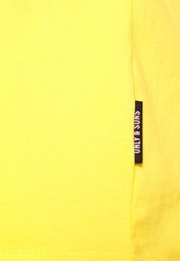 Żółta bawełniana koszulka z ribbową fakturą oraz boczną metką z napisem "UNLY & SUNS". Prosty design, bez wzorów i dodatkowych akcentów.