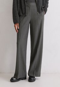 Hulahup hlače širokog kroja visokog struka od tamnosivog materijala, s utisnutim pregibima i bočnim džepovima, uparenim s crnim platformama.