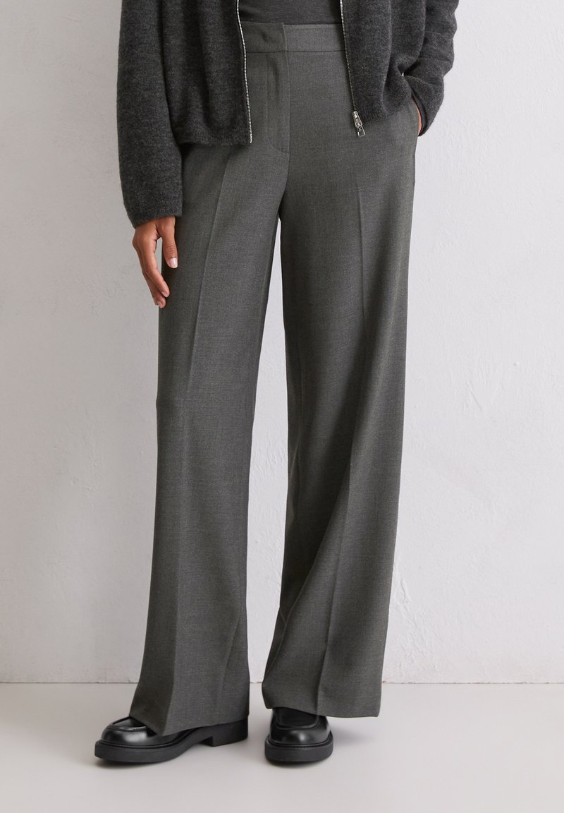 Vysoké, široké nohavice v tmavosivej tkanine, so zažehlenými skladačkami a bočnými vreckami, v kombinácii s čiernymi platformovými topánkami.