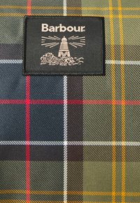 Barbour brand label with lighthouse logo on fabric featuring green, blue, red, white, and yellow tartan plaid pattern.