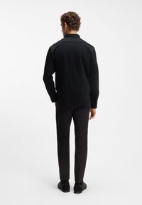 Μαύρο πουκάμισο με κουμπιά, μακρυμάνικο, εφαρμοστή γραμμή και ομαλή υφή υφάσματος, συνδυασμένο με μαύρο παντελόνι και παπούτσια. Εμφανίζεται η πίσω όψη.