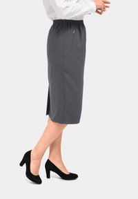 Grijze knielange rok met elastische tailleband, voorzien van een zijrits zak en een zijsplit. Gecombineerd met zwarte hoge hakken.