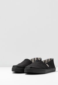 Svarta kanvas slip-on skor med en texturerad yta, gummisula och randig tygfoder. Har en rundad tå och en minimalistisk design.