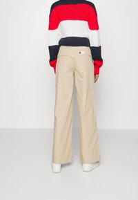 Beige kalhoty s širokými nohavicemi vyrobené z bavlny, s dvěma zadními kapsami a značkovou nášivkou, v kombinaci s horizontálně pruhovaným svetrem v červené, bílé a námořnické modři.