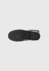 Suela de bota de cuero negro con textura estriada, forma redondeada y ligera elevación. Presenta un diseño minimalista y un acabado suave.