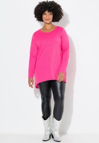 Tunique à manches longues rose vif avec un col rond et un ourlet asymétrique. Associée à des leggings noirs brillants et des bottes de cowboy métalliques argentées.