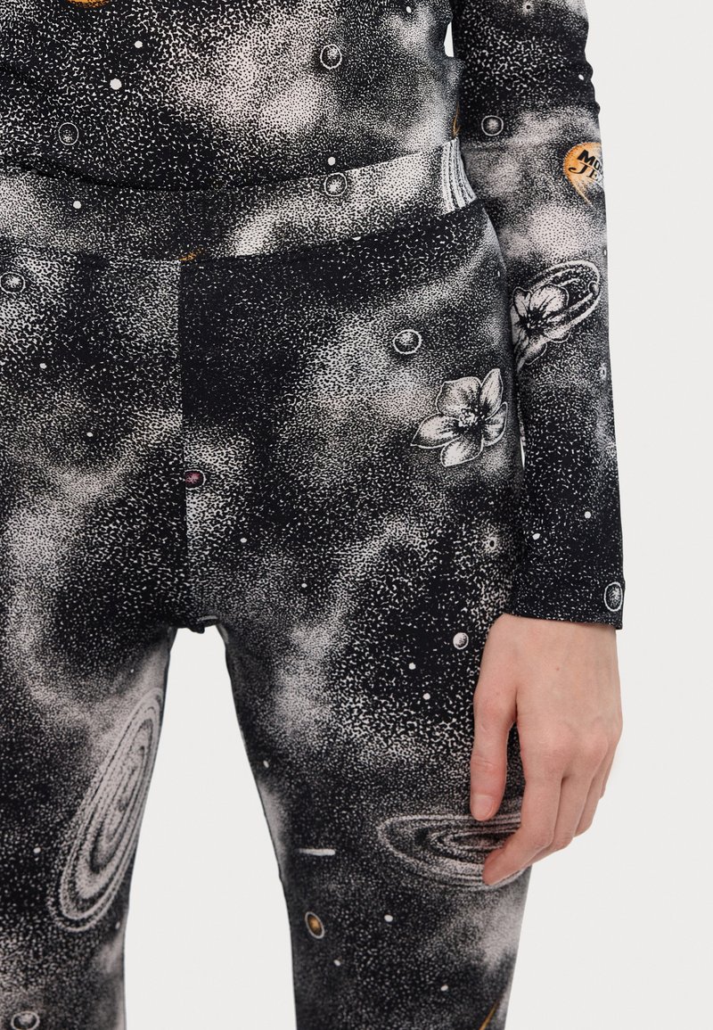 Leggings negros con un patrón galáctico que presenta manchas blancas, planetas y diseños florales; fabricados con una tela elástica y texturizada.