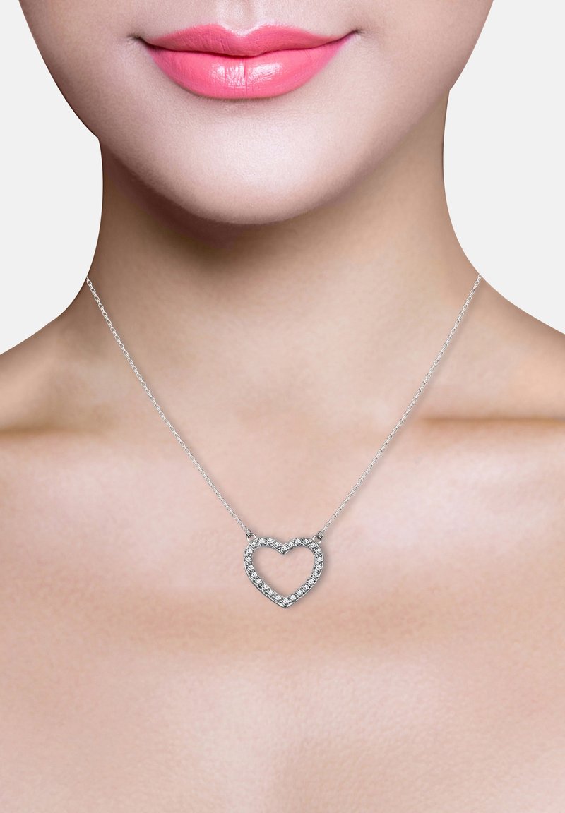 Silberne Herz-Kette mit hohlem Zentrum, verziert mit kleinen klaren Edelsteinen, hängt an einer zarten Kette vor einem neutralen Hintergrund.