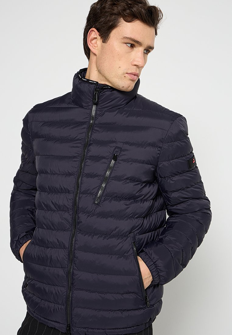 Marineblauwe pufferjack met een horizontaal doorgestikt ontwerp, hoge kraag, zwarte ritssluitingen en zijzakken. Zachte textuur en lichtgewicht materiaal.