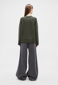 Tume roheline kootud kampsun soonikkoes äärte ja varrukate küljes, kombineeritud laia halli püksiga. Kampsunil on tagumine õmblus ja väike logo detail.