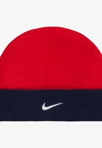 Rød strikket lue med marineblå brett som har en hvit Nike-logo, utstyrt med en myk tekstur og rund topp.