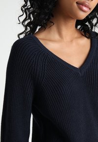 Navyblauwe gebreide trui met een V-hals ontwerp, featuring een gestructureerde ribbels en een getailleerd silhouet.