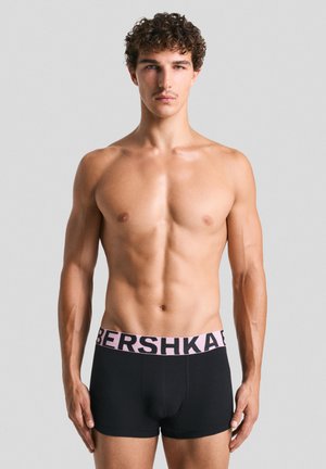 Černé boxerské šortky s růžovým pasem s logem "BERSHKA". Hladká látka, přiléhavý střih a délka do půli stehna. Model je bez trička.