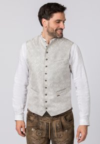 Hellgraue Weste mit Muster und hohem Kragen, sechs Knöpfen und zwei seitlichen Taschen. Kombiniert mit einem weißen Langarmhemd und braunen Hosen.