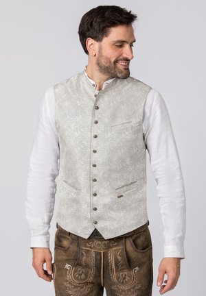 Hellgraue Weste mit Muster und hohem Kragen, sechs Knöpfen und zwei seitlichen Taschen. Kombiniert mit einem weißen Langarmhemd und braunen Hosen.
