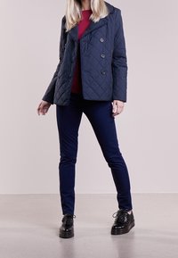 Marinblå vadderad dubbelknäppt jacka, röd topp, marinblå slim-fit byxor och svarta snörskor med texturerade detaljer. Enkel och modern design.