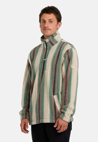 Fleece pullover in groen, crème en roestkleurige strepen. Heeft een ritssluiting, staande kraag en zijzakken. Getextureerde, warme stof.