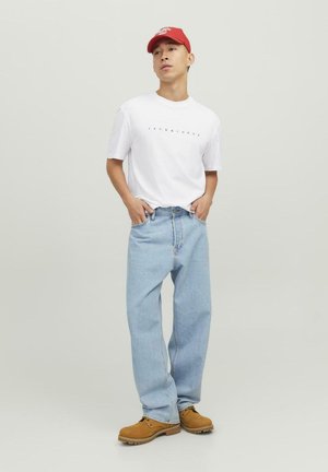 White t-shirt with black logo, light blue baggy jeans, and brown work boots. Red baseball cap. Simple design, casual fit, and denim texture.