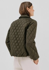 Giacca trapuntata verde oliva con colletto, caratterizzata da motivi a diamante, maniche lunghe e una silhouette aderente. Materiale liscio e lucido.