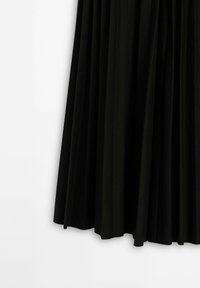 Jupe plissée noire suspendue sur un fond blanc, montrant la texture du tissu et les plis drapés.