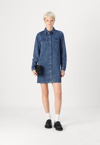 Jeansskjol med knappstängning, långa ärmar, bröstfickor och rak silhuett. Bärs med svarta skor och en liten svart väska.