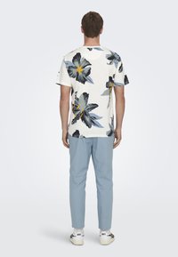 Hvit kortermet skjorte med svart og blå blomsterdesign, paret med lyseblå bukser og hvite sneakers.