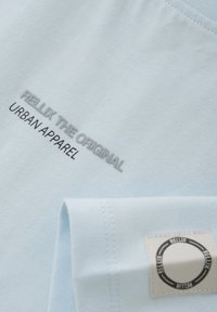 Lyseblå bomulds T-shirt med grå broderet tekst "RELLIX THE ORIGINAL URBAN APPAREL" og et rektangulært mærke på ærmet.