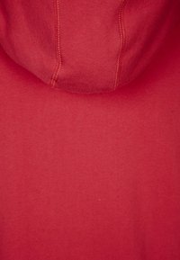 Sudadera con capucha roja de textura suave de algodón, con capucha ajustable mediante cordón y costuras visibles. El color es uniforme en toda la prenda.