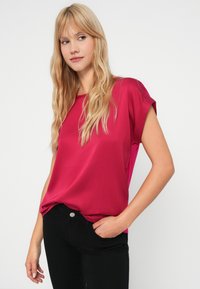 Fuchsia silketopp med korte, rullede ermer, rund hals, og en avslappet passform, parret med tettsittende svarte jeans. Glatt tekstur.
