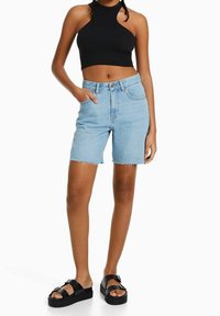 Helle blaue Denim-Shorts mit fransigen Säumen, hoher Taille und einer vorderen Knopfverschlüsse. Kombiniert mit einem schwarzen gerippten Crop-Top und schwarzen Sandalen.