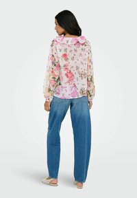 Blusa floral transparente con cuello rizado, con flores rosas y moradas sobre un fondo claro. Combinada con jeans sueltos de color azul claro.