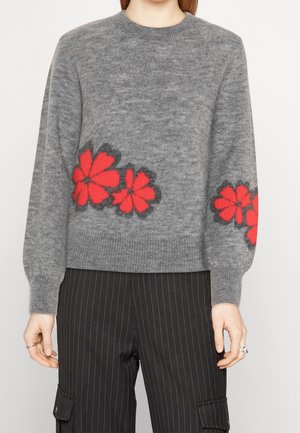Suéter gris de punto con patrones florales rojos y negros en el frente y las mangas, combinado con pantalones cargo de rayas negras.