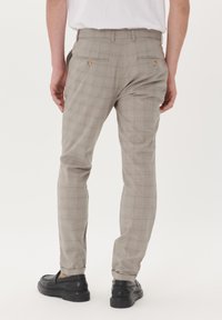 Helle grau karierte Hose mit maßgeschneidertem Schnitt, aus glattem Stoff, mit zwei Gesäßtaschen und Knopfdetails. Kombiniert mit schwarzen Schuhen.