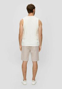 Männer ärmelloses weißes Tanktop und beige Shorts, kombiniert mit weißen Sneakern. Weicher Stoff, lockere Passform, einfaches Design und neutrales Farbschema.
