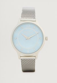 Ρολόι με ασημένια πλέξη διορθωτή με ανοιχτό μπλε καντράν, που διαθέτει ασημί δείκτες ωρών και λογότυπο. Στρογγυλή κάσα με λεία επιφάνεια και κορώνα.