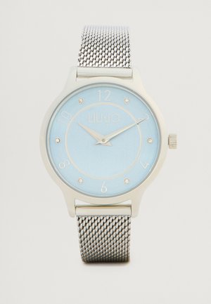Orologio con cinturino in maglia d'argento e quadrante blu chiaro, dotato di indicatori delle ore in argento e di un logo. Cassa rotonda con finitura liscia e corona.