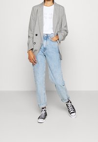 Šedý kostkovaný blazer, bílý tričko s potiskem, světlemodré džíny s vysokým pasem a černé tenisky s bílou podrážkou. Neformální outfit.