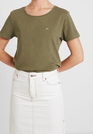 Vrouw draagt een olijfgroen T-shirt met korte mouwen, ingestopt in een witte, hooggetailleerde denimrok met knopen aan de voorkant en stikseldetails.