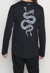 Czarna koszulka z długim rękawem z srebrnym wzorem węża na plecach z napisem. Z przodu brak grafik; miękki materiał o luźnym kroju.