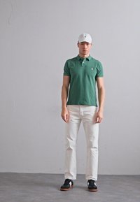 Roheline polo särk, valged teksad ja mustad sneakers valgete aktsentidega. Polo on klassikalise lõikega ning rinna peal on väike logo.