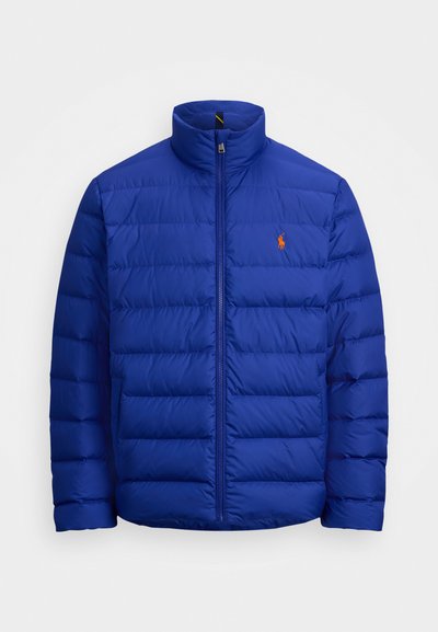 Zils pūkains jaku ar augstu apkakli, rāvējslēdzēja priekšpusi un horizontālu quilted rakstu. Tam ir neliels oranžs logo kreisajā krūtī.