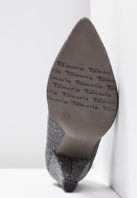 Talon haut en tissu pailleté argenté avec un bout pointu. Marque distinctive sur la semelle extérieure avec l'étiquette de taille 37 clairement visible.