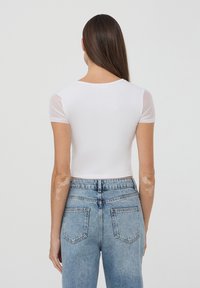 T-shirt bianco cropped con maniche corte in rete trasparente, texture liscia, scollatura rotonda, abbinato a jeans in denim azzurro chiaro a vita alta.
